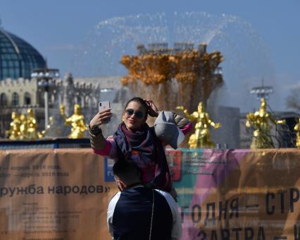 Москва. Девушка делает селфи на фоне фонтана `Дружба народов` на ВДНХ.