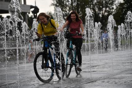 Москва.  Девушки катаются на велосипедах среди фонтанов  Крымской набережной.