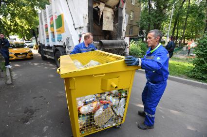 Москва.   Рабочие грузят мусорный контейнер.