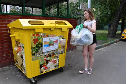 Москва.   Девушка выбрасывает мусор в мусорный контейнер.