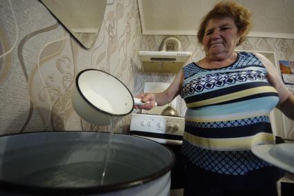 Екатеринбург. Бабушка в своем дачном домике набирает питьевую воду из большой кастрюли