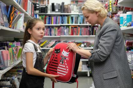 Санкт-Петербург.   Женщина с девочкой выбирают рюкзак в отделе школьных принадлежностей в магазине канцтоваров перед началом учебного года.