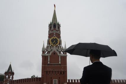 Москва. Мужчина в костюме под зонтом на Красной площади смотрит на Спасскую башню Кремля.