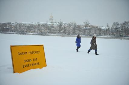 Екатеринбург. Дети идут по льду городского пруда мимо арт-объекта, дорожного знака с надписью \'Знаки повсюду\' во время снегопада