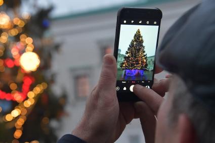 Москва.   Мужчина фотографирует новогоднюю елку на Соборной площади Кремля.