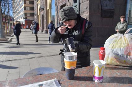 Москва. Пожилая женщина ест  на Тверской улице.