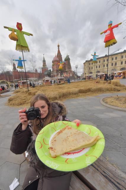 Москва. Девушка с блинами  на фоне чучела Масленицы в парке Зарядье.