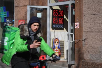 Москва. Сотрудник службы доставки еды у обменного пункта валюты.