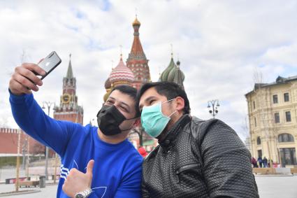 Москва.  Молодые люди в медицинских масках фотографируются у храма Василия Блаженного.