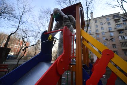 Москва. Сотрудник коммунальной службы в защитном костюме и респираторе во время дезинфекции детской площадки.