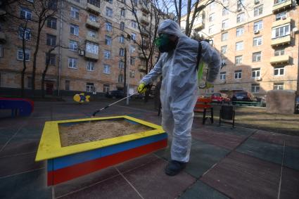 Москва. Сотрудник коммунальной службы в защитном костюме и респираторе во время дезинфекции детской площадки.