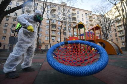 Москва. Сотрудник коммунальной службы в защитном костюме и респираторе во время дезинфекции детской площадки.