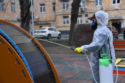 Москва. Сотрудник коммунальной службы в защитном костюме и респираторе во время дезинфекции детской площадки.