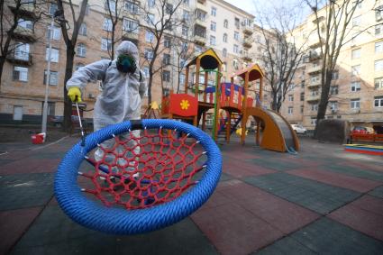 Москва. Сотрудник коммунальной службы в защитном костюме и респираторе во время дезинфекции детской площадки.