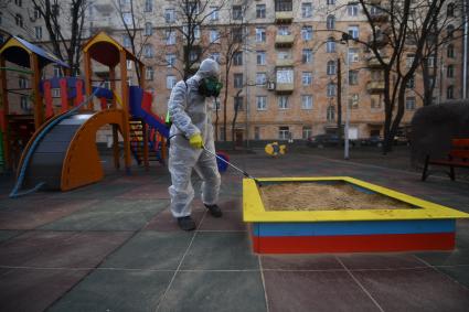 Москва. Сотрудник коммунальной службы в защитном костюме и респираторе во время дезинфекции детской площадки.