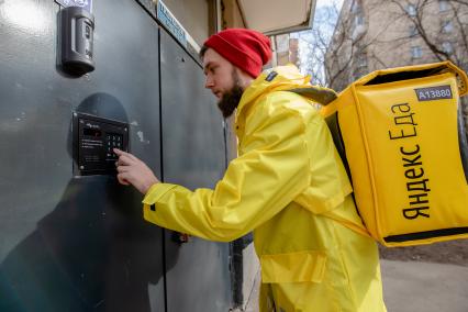 Москва.   Сотрудник сервиса по доставке еды `Яндекс Еда` у подъезда дома.