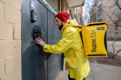 Москва.   Сотрудник сервиса по доставке еды `Яндекс Еда` у подъезда дома.