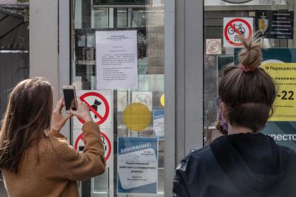 Москва.   Девушка фотографирует на мобильный телефон объявление о закрытии торгового центра.