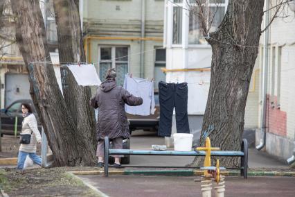 Москва.   Женщина развешивает белье во доре дома.