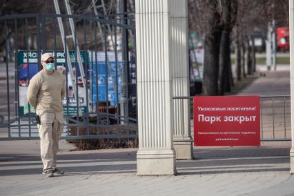 Москва.  Мужчина  в медицинской маске у ворот закрытого парка.