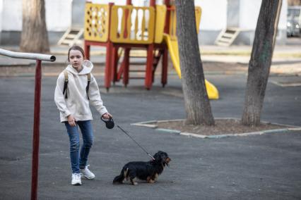 Москва.   Девочка гуляет с собакой во дворе дома.