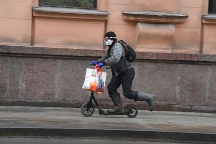 Москва. Мужчина в медицинской маске и резиновых перчатках на самокате.