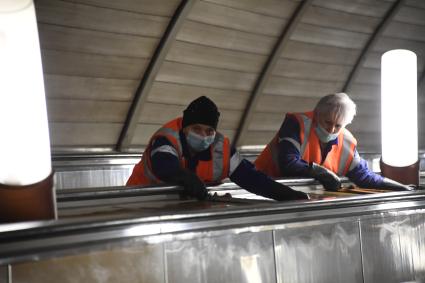 Москва. Сотрудники метрополитена дезинфицируют перила эскалатора.