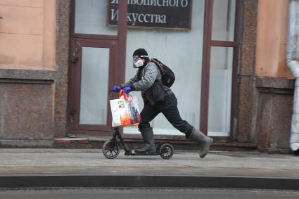 Москва. Мужчина в медицинской маске и резиновых перчатках на самокате.