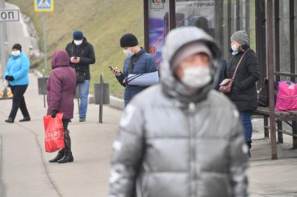 Москва.  Люди в медицинских масках на остановке общественного транспорта.