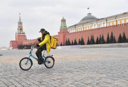 Москва. Сотрудник сервиса доставки еды `Яндекс. Еда`едет по Красной площади на велосипеде.