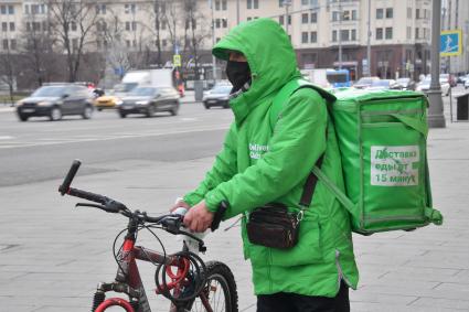 Москва. Сотрудник сервиса доставки еды в медицинской маске на улице города.