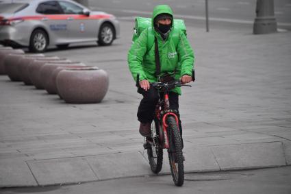 Москва. Сотрудник сервиса доставки еды в медицинской маске на улице города.