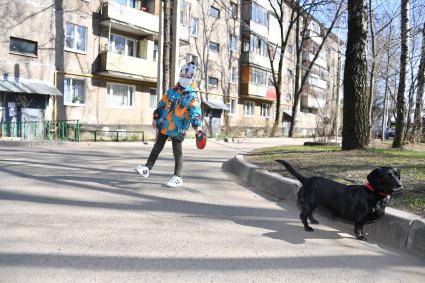 Москва.   Мальчик в медицинской маске гуляет с собакой во дворе.