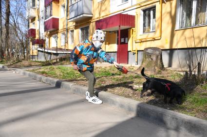 Москва.   Мальчик в медицинской маске гуляет с собакой во дворе.