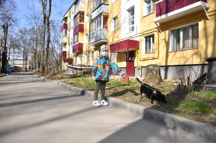 Москва.   Мальчик в медицинской маске гуляет с собакой во дворе.