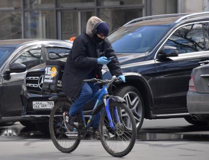 Москва. Мужчина на велосипеде в медицинской маске на улице города.