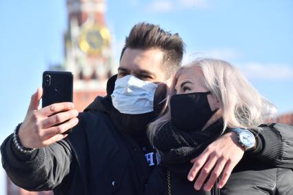 Москва. Молодой человек и девушка в медицинских масках фотографируются  на  Красной площади