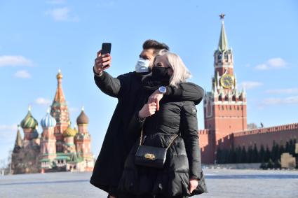 Москва. Молодой человек и девушка в медицинских масках фотографируются  на  Красной площади