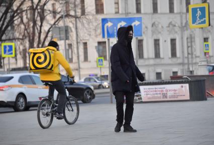 Москва. Сотрудник сервиса доставки еды на велосипеде и  прохожий в медицинской маске.