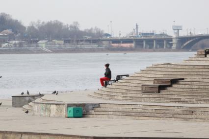 Иркутск. Женщина в медицинской маске сидит одна на набережной Ангары.