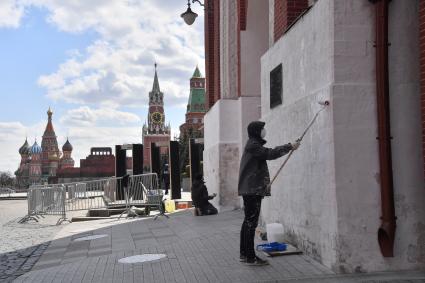 Москва. Рабочий в медицинской маске красит стену дома.