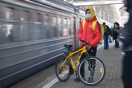 Москва. Сотрудник сервиса доставки еды  в медицинской маске  с велосипедом на платформе пригородных поездов.