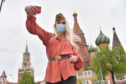 Москва.  Девушка в медицинской маске делает селфи на Красной площади во время празднования Дня Победы.