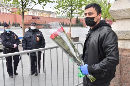 Москва.  Мужчина в медицинской маске и перчатках с цветами  на Красной площади во время празднования дня Победы.