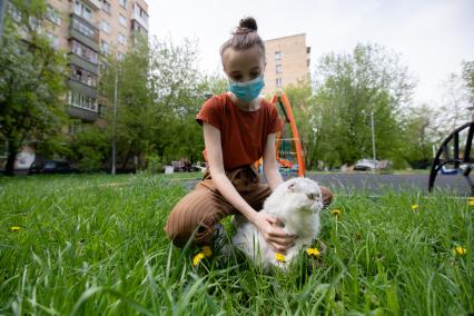 Москва. Девушка в медицинской маске гуляет с кошкой во дворе.