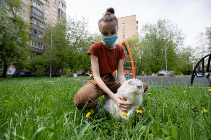 Москва.  Девушка в медицинской маске гуляет с кошкой во дворе.