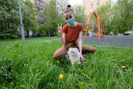 Москва.  Девушка в медицинской маске гуляет с кошкой во дворе.