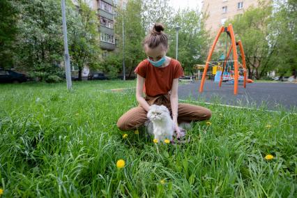 Москва.  Девушка в медицинской маске гуляет с кошкой во дворе.