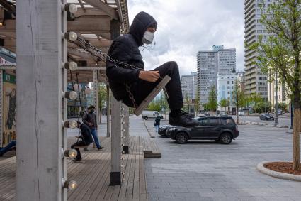 Москва. Молодой человек в медицинской маске на качелях на Новом Арбате.
