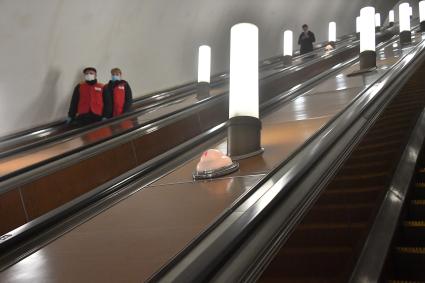 Москва. Женщина и мужчина в медицинских масках на эскалаторе в метро.